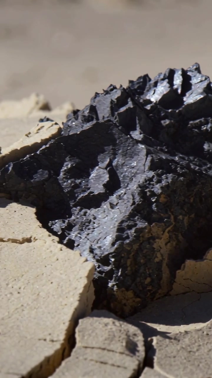 Vertical video: Pulling back camera revealing dark jagged rock on cracked mud, sun showing texture