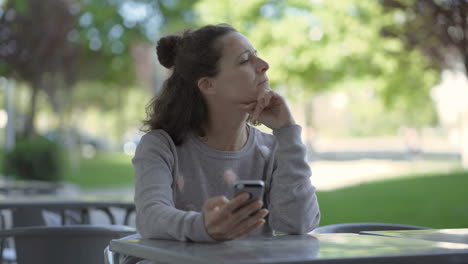 thoughtful mature woman sitting at table with smartphone.