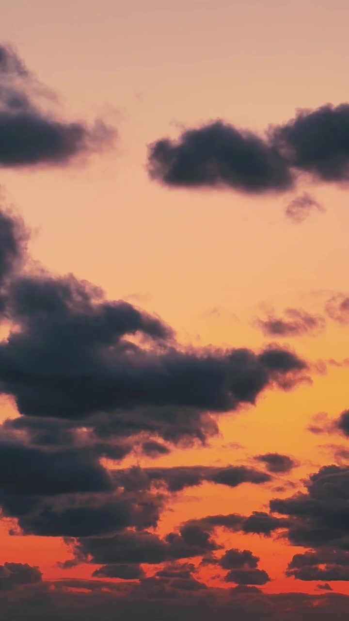 Static shot of a warm golden sunset sky as dark clouds drift slowly by.