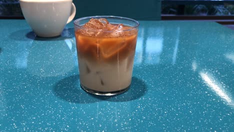 glass of cold brew and milk in separated layers with ice cubes on a turquoise table