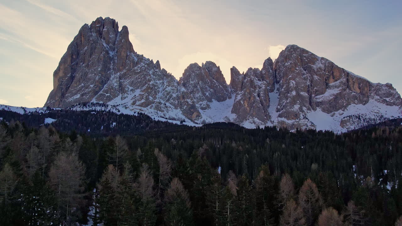 impresionantes picos de montañas nevadas que se elevan sobre un denso bosque al anochecer, con un hermoso cielo crepúsculo en el fondo
