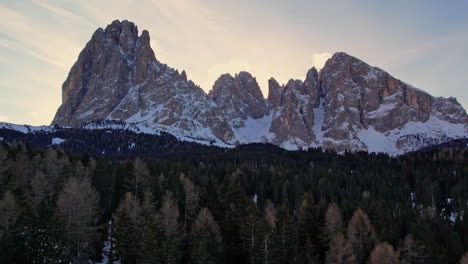 stunning snowy mountain peaks towering over a dense forest at dusk, with a beautiful twilight sky in the background