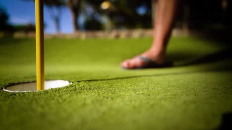 mini bola amarela de golfe com um bastão perto do buraco ao pôr do sol