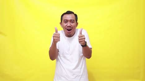 happy man, dancing and thumbs up in success, good job or winning against a yellow studio background