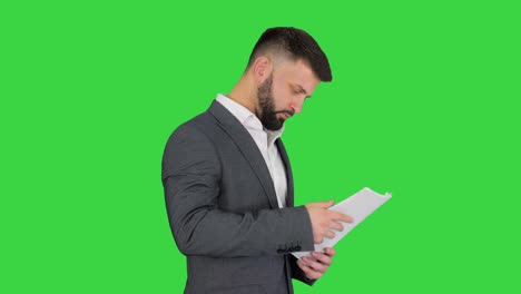 hombre de negocios turco de pie y mirando documentos en una pantalla verde, clave de croma