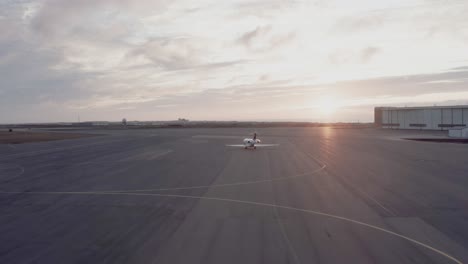 business jet departing on open tarmac of airport at dusk, taxiing towards runway