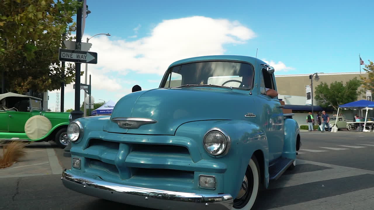 Bright blue Chevrolet pickup drives past car show