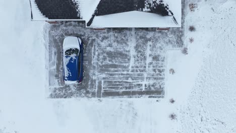 top down aerial shot of a car covered in snow sitting in a suburban driveway