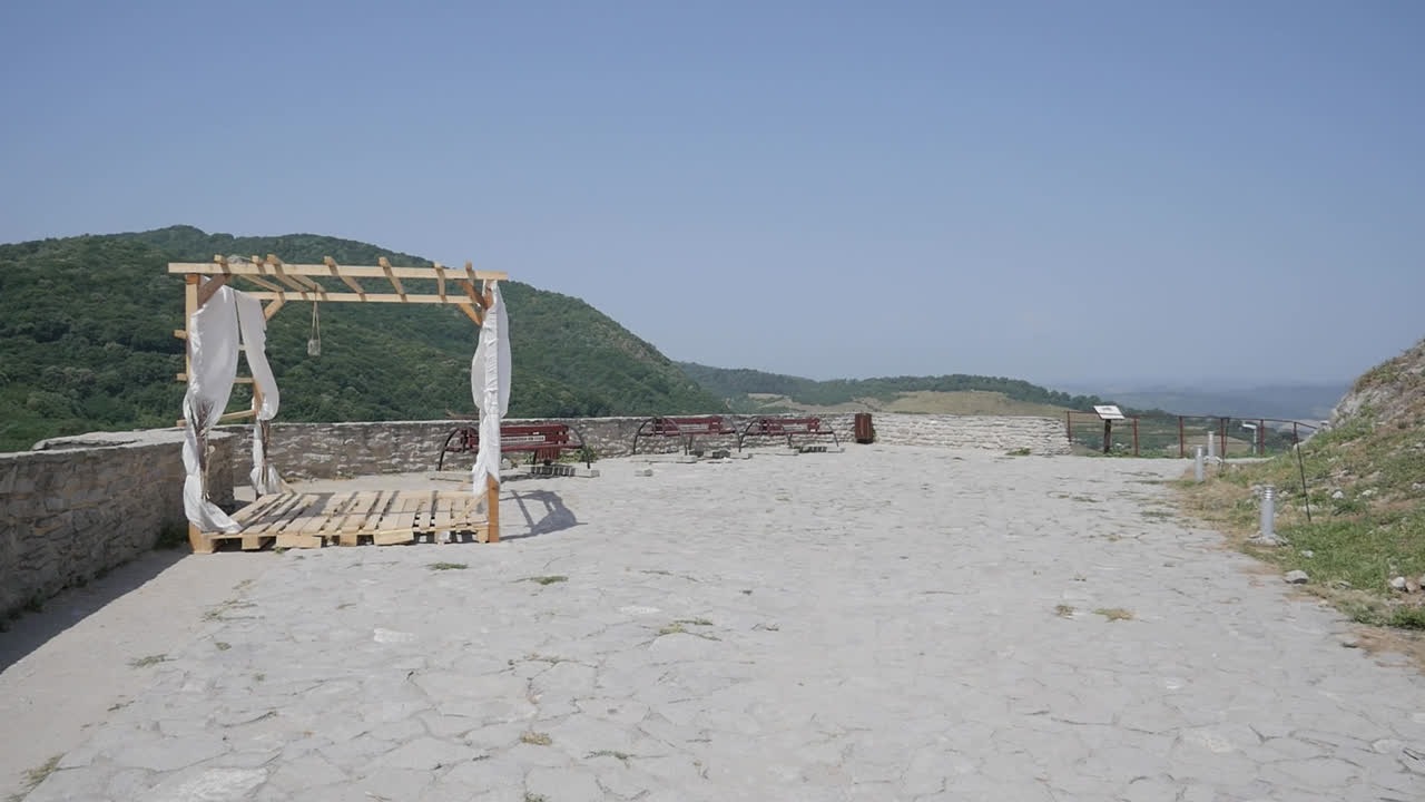 Dry landscape with wooden swing structure and mountain backdrop in bright sunlight, sacred marriage venue overlooking ocean