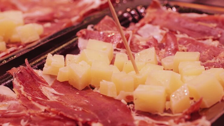 Fette di prosciutto e cubetti di formaggio su un vassoio da portata nero, ottimi per eventi di catering o riunioni