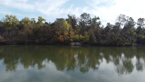drone floating along the surface of still teal blue water with tree reflecting on the surface in the distance