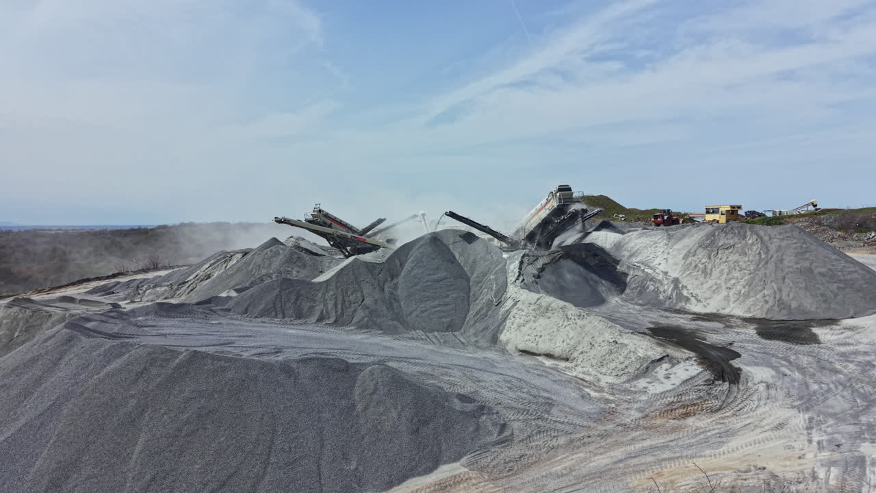 Actividad en una cantera de granito, con maquinaria moviendo materiales pétreos y grandes montones de granito al fondo.