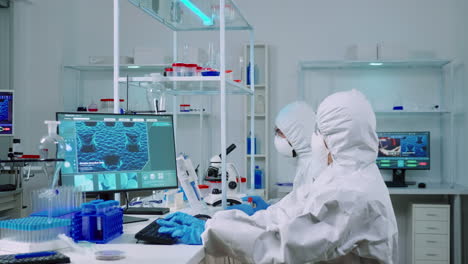 químico escribiendo en la computadora y compañero de trabajo analizando diapositivas de microscopio