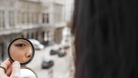 Woman-looking-through-compact-mirror,-Vienna-State-Opera-blurred-in-background,-overcast-light