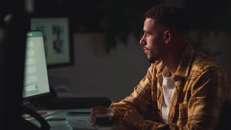 businessman working late in office with face illuminated by computer screen drinking coffee