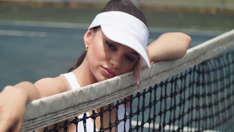 Young-latina-holds-her-face-next-to-the-net-at-a-tennis-court
