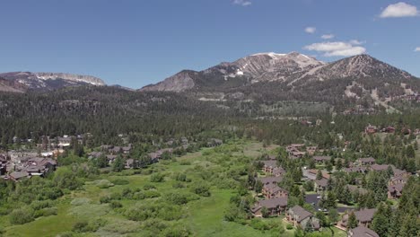 La-Cámara-De-Imágenes-De-Drones-De-4k-Se-Inclina-Hacia-Abajo-De-La-Hermosa-Montaña-Gigantesca-En-Verano-Con-Vistas-A-Un-Exuberante-Prado-Verde-Y-Cabañas