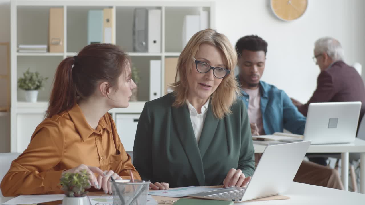 Middle-Aged Female Supervisor Training New Employee in Busy Office