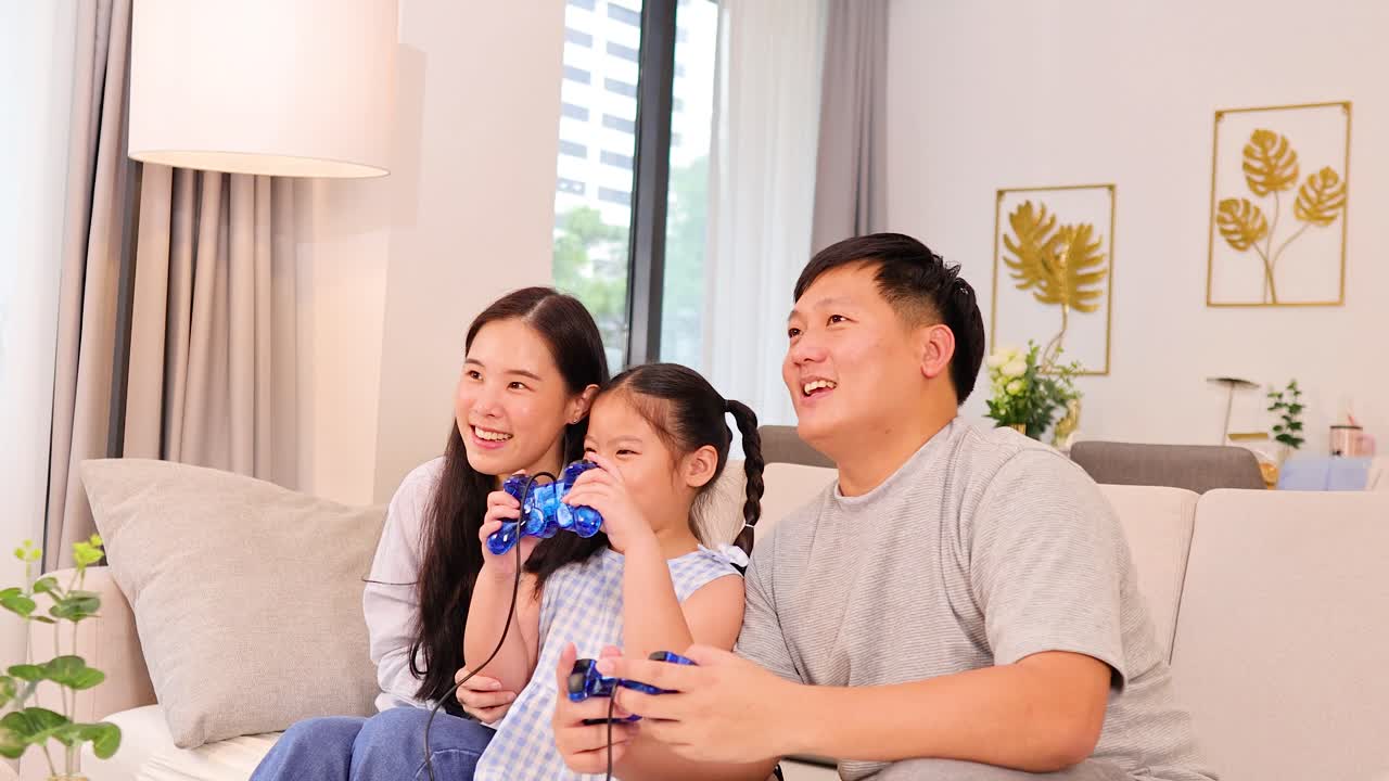 Parents and daughter enjoy video gaming on couch, bright natural lighting, cheerful and relaxed atmosphere