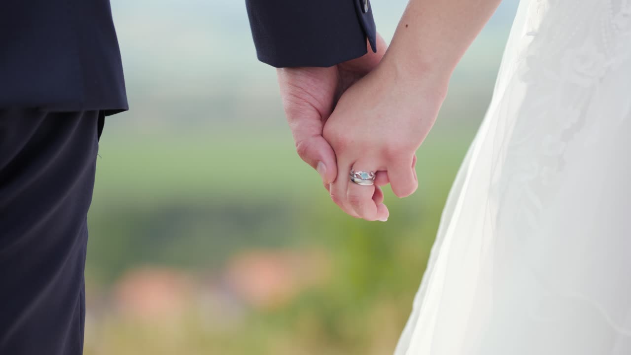 新娘和新郎站在自然草原外面握手, 手上有模糊的背景和婚戒