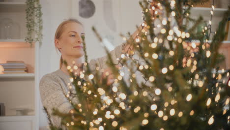 woman decorating christmas tree with glowing led lights