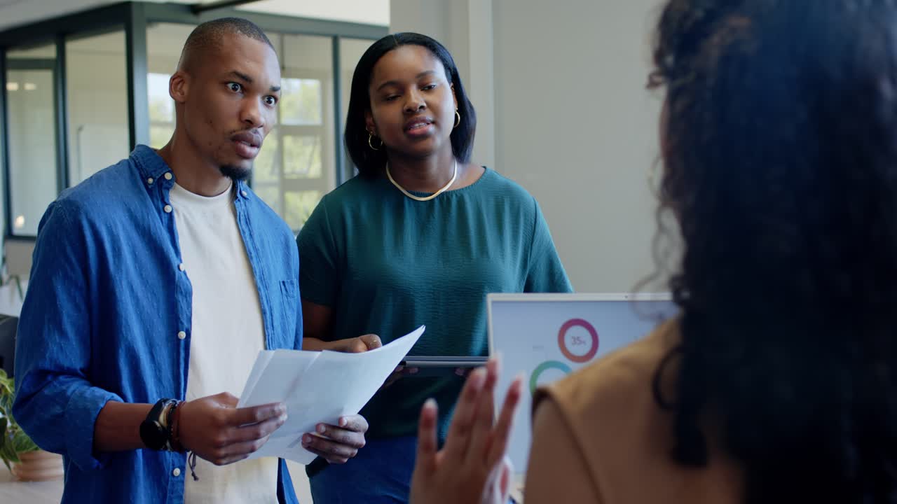 African American team reviewing papers on data as presenter raising finger gesturing in office