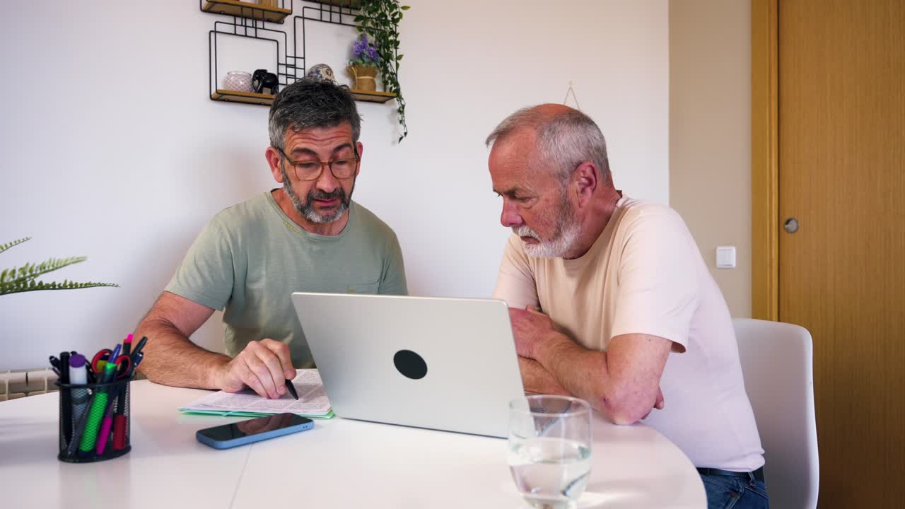 Two Men Collaborating on Laptop and Documents at Home