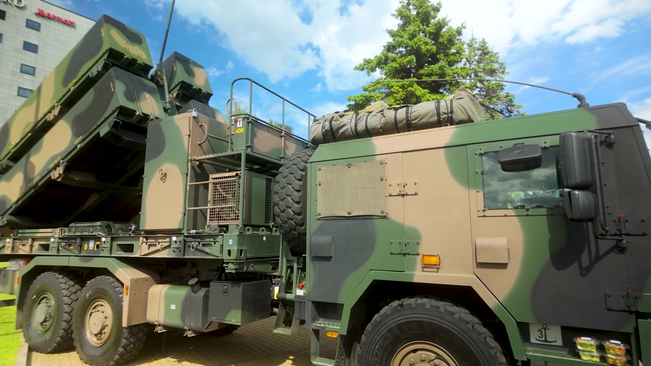 Et tungt militærkjøretøy utstyrt med et bakke-til-luft missilsystem, parkert under en offentlig utstilling. Egnet for forsvars-, sikkerhets- og geopolitisk nyhetsinnhold.