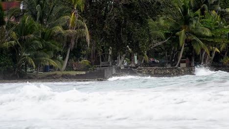 grandes olas largas rompiendo en tierra y salpicando en las rocas frente al bosque tropical de palmeras