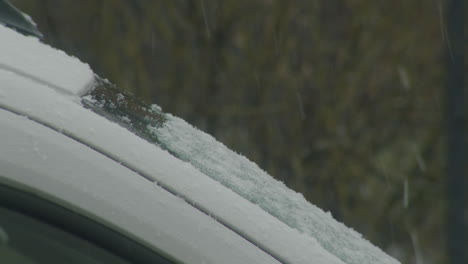 static close up shot of a cars windshield, view from the side. snow falling. windshield covered a little bit.