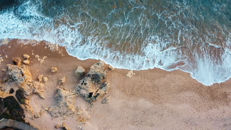 Arial-view-of-Portugal's-rugged-coastline,-with-the-tranquil-sea-waves-gently-caressing-the-rocky-formations-bathed-in-the-radiant-of-a-delightful-day