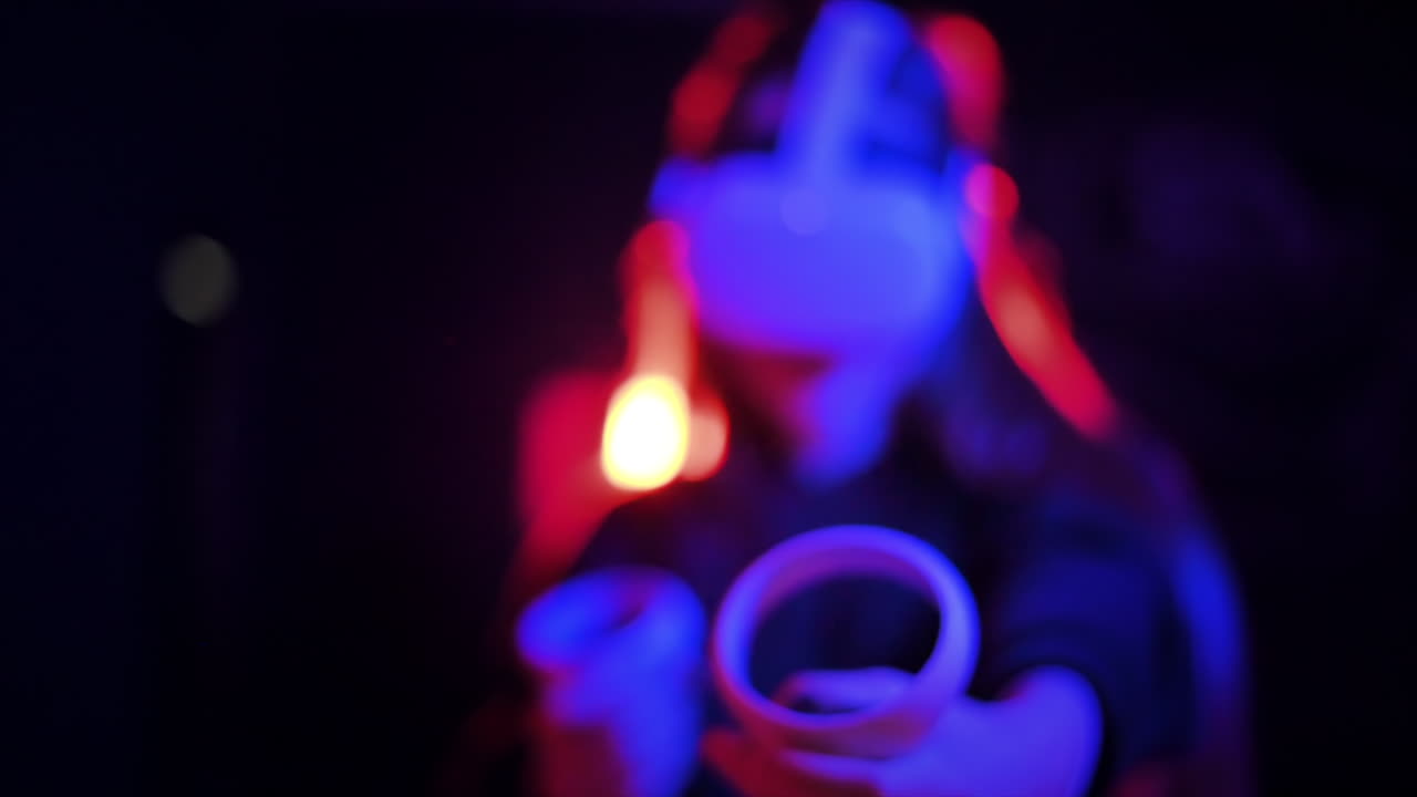 Una giovane donna interessata gioca a giochi di realtà virtuale usando occhiali e controller VR. Illuminazione rossa e blu. Rallentatore