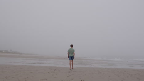 boy walking alone on a foggy beach