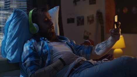man relaxing in bedroom with headphones and smartphone
