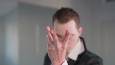 man with neck tattoo raises hand to face in bold gesture, partially obscuring expression, framed by mirror reflection and minimalist studio setting with soft light and modern neutral walls