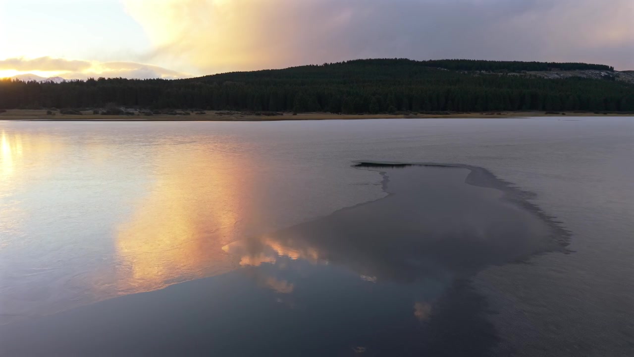 Esquel'deki donmuş Laguna La Zeta, canlı turuncu kış şafağında. Kalın buzun üzerinden geçen, arka plandaki karanlık ormana yaklaşan alçak ileri havadan çekim