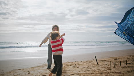 Madre-Hijo-Lanzando-Cometa-En-La-Ventosa-Costa-Del-Océano.-Mujer-Alegre-Ayudando-A-Niño