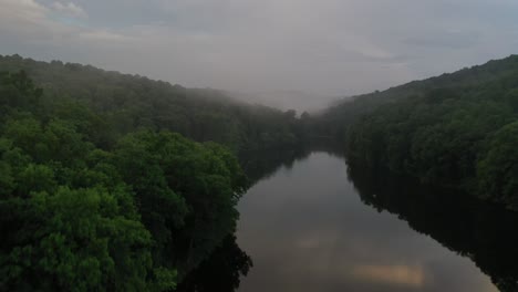 narrow forest river with rising fog in early summer morning, aerial view