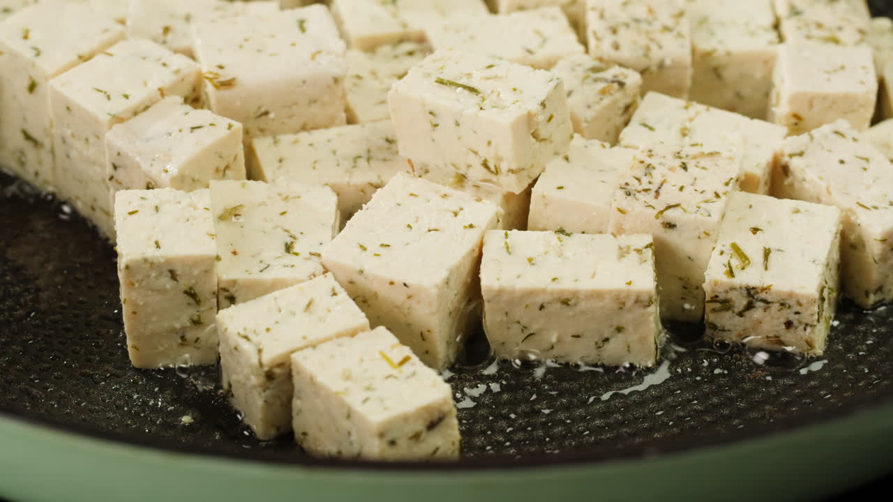 Fried tofu with sesame seeds and spices on cast iron pan, cooking japanese salad. Healthy ingredient for cooking vegan vegetarian diet food. Roasted tofu over black background.