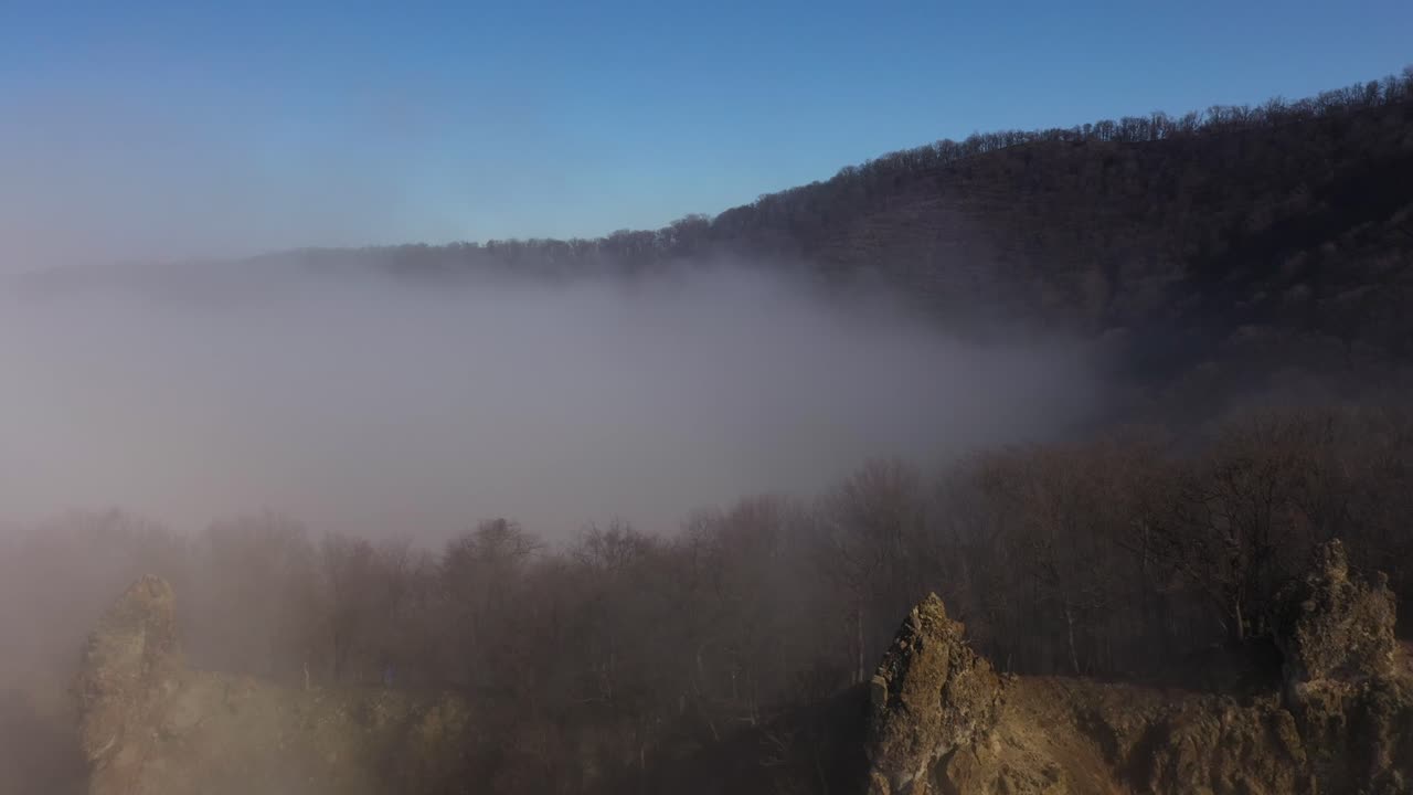 Drone flying over the hill in the foggy sunny winter