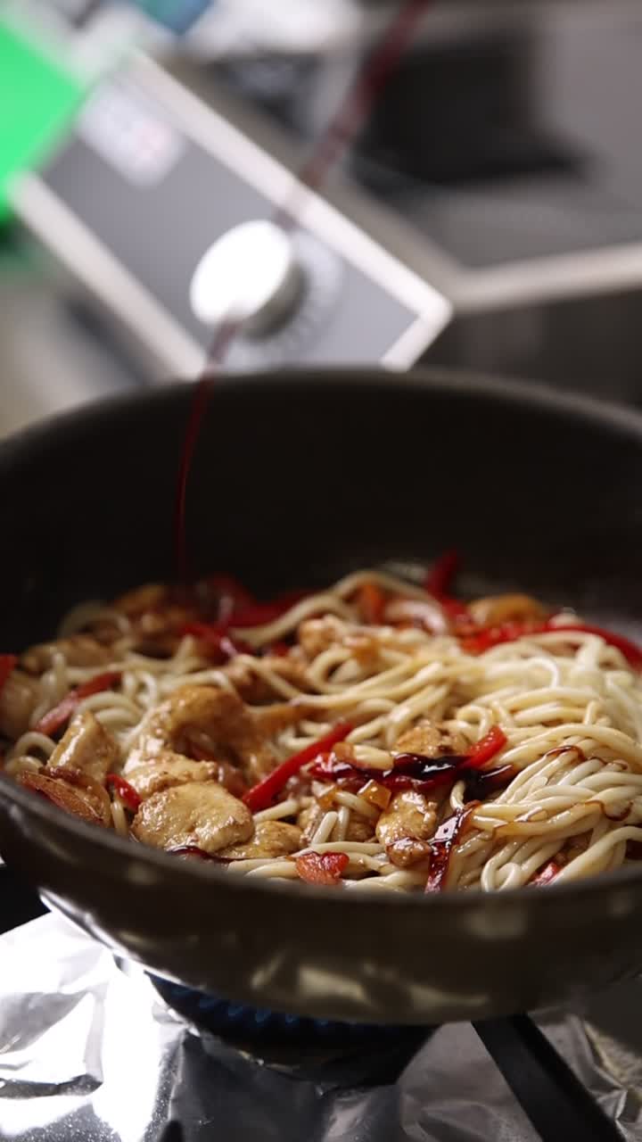 フライパンの鶏肉とピーマンが入った麺にソースをかける