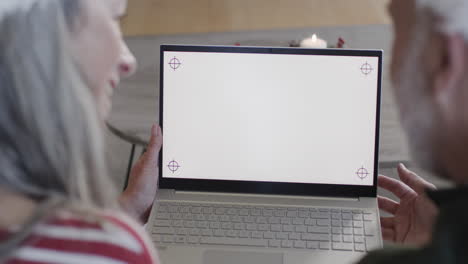 una pareja caucásica de mediana edad con una computadora portátil con pantalla en blanco en navidad en casa, en cámara lenta