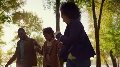 parents helping kid riding longboard holding hands evening autumn park closeup.