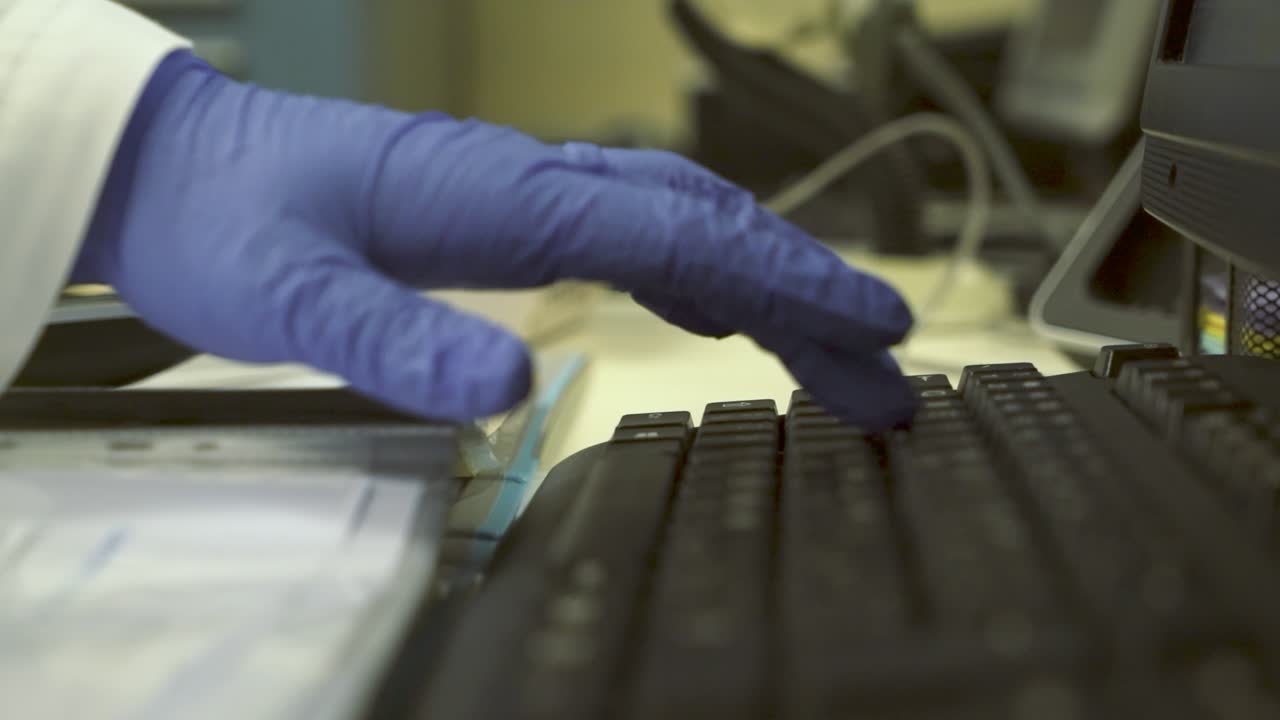 의료 실험실에서 컴퓨터의 키보드에 입력하는 파란색 라텍스 장갑을 끼고 실험실 기술자