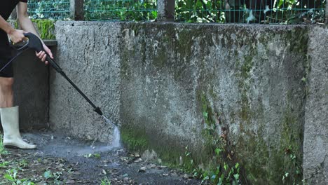 Caucasian-man-with-boots-uses-pressure-washer-to-clean-moss-off-wall