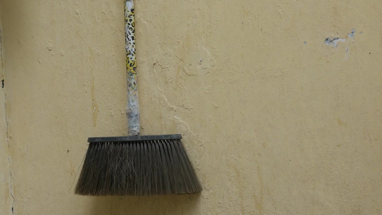 Koště opřené o zeď v jednoduchém venkovním prostředí, detailní záběr.