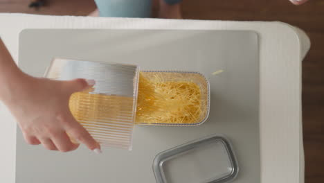 female hands pour raw spaghetti into plastic container