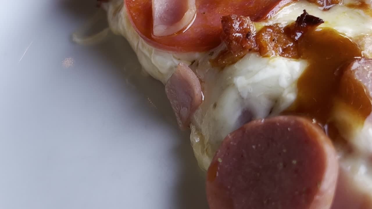 Close up shot of pizza on a plate with ham, cheese and chorizo, handheld
