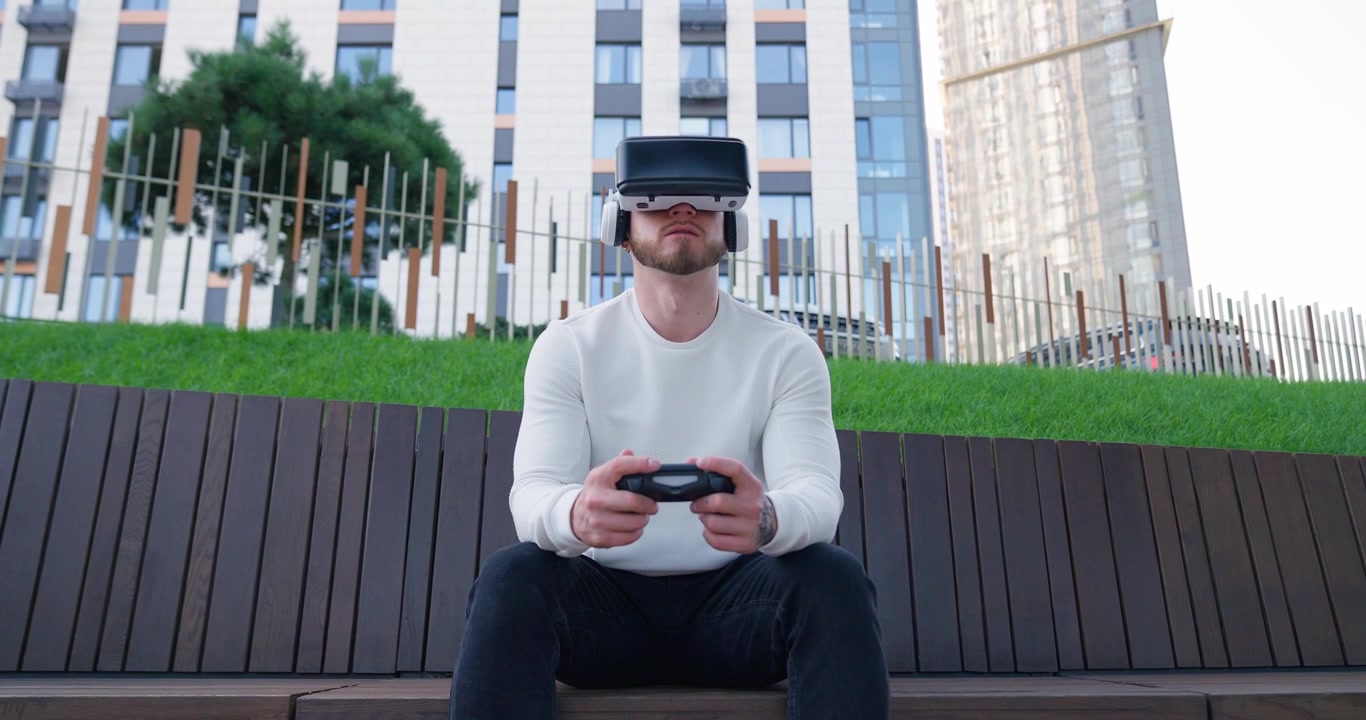 Giovane uomo che gioca a un gioco di realtà virtuale su una panchina in città