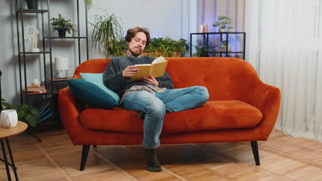 bearded man reading interesting book turning pages smiling enjoying literature taking a rest at home